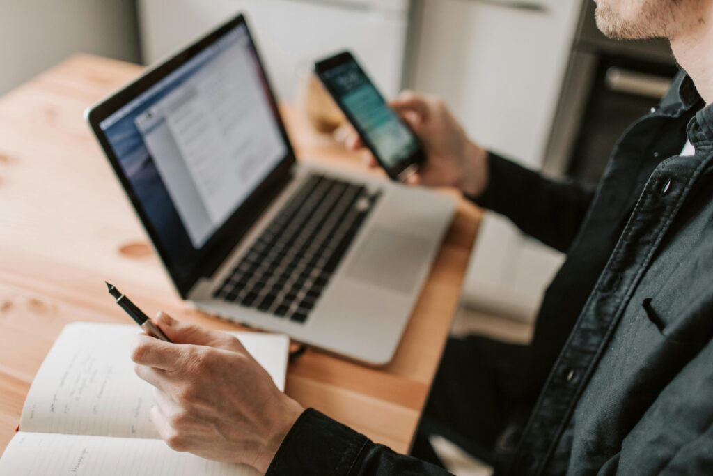 pexels-photo-4050451-4050451 A person multitasking with a laptop and smartphone at a wooden desk.